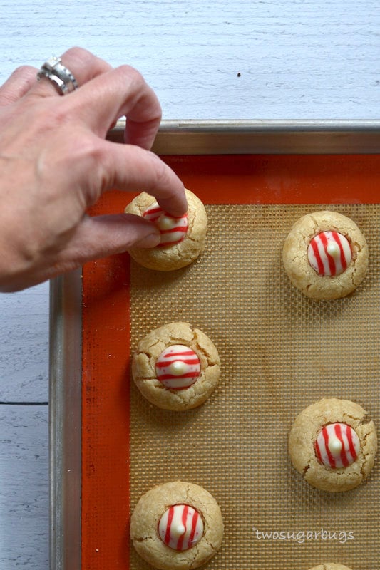 hand placing a white chocolate candy cane kiss into a cookie