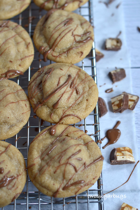 peanut butter snickers cookies with drizzled chocolate on a wire cooling rack