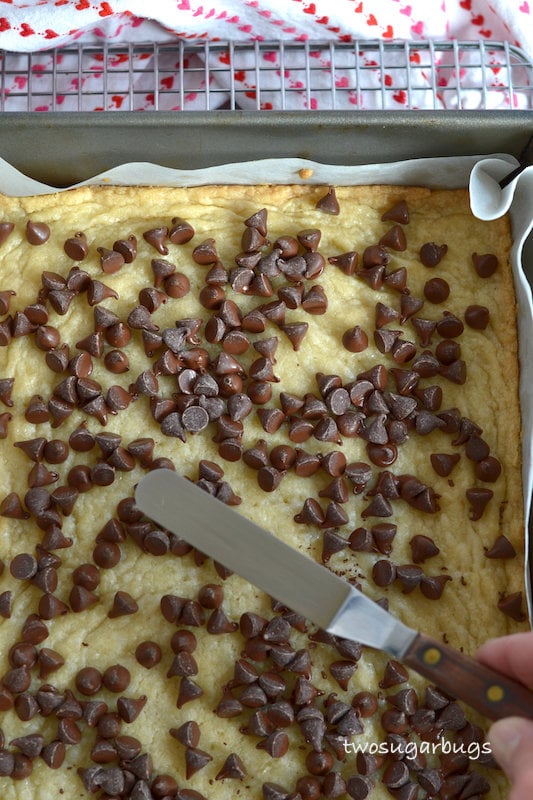baked cookie base with softened chocolate chips being spread with an offset spatula