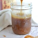 Mason jar of whiskey vanilla caramel sauce with a spoon dripping sauce back into the jar