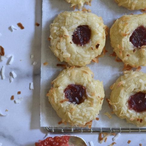 Coconut jam thumbprints on a cooling rack with a jam filled spoon
