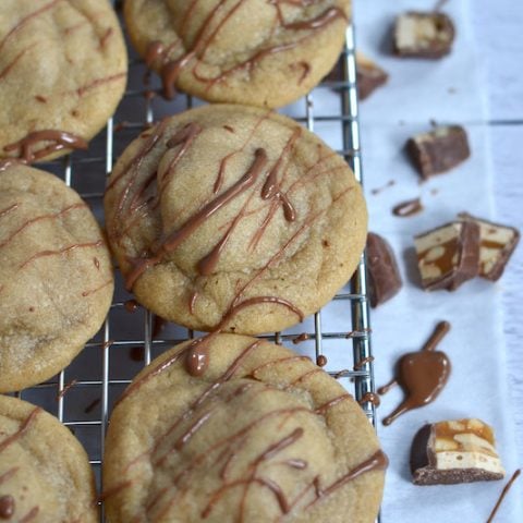 peanut butter snickers cookies with drizzled chocolate on a wire cooling rack