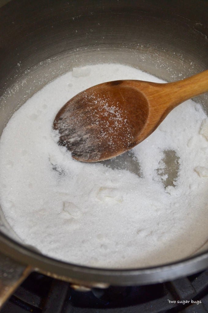 sugar in a sauce pan with a wooden spoon in the initial melting stage