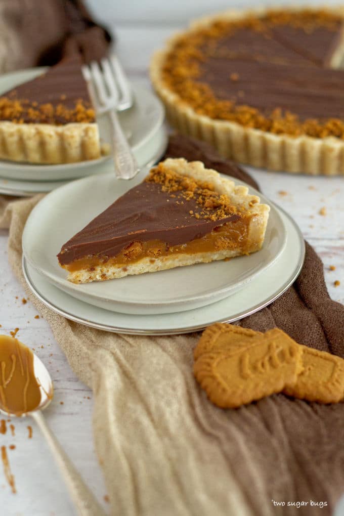 slice of biscoff caramel tart on three plates with full tart in the background