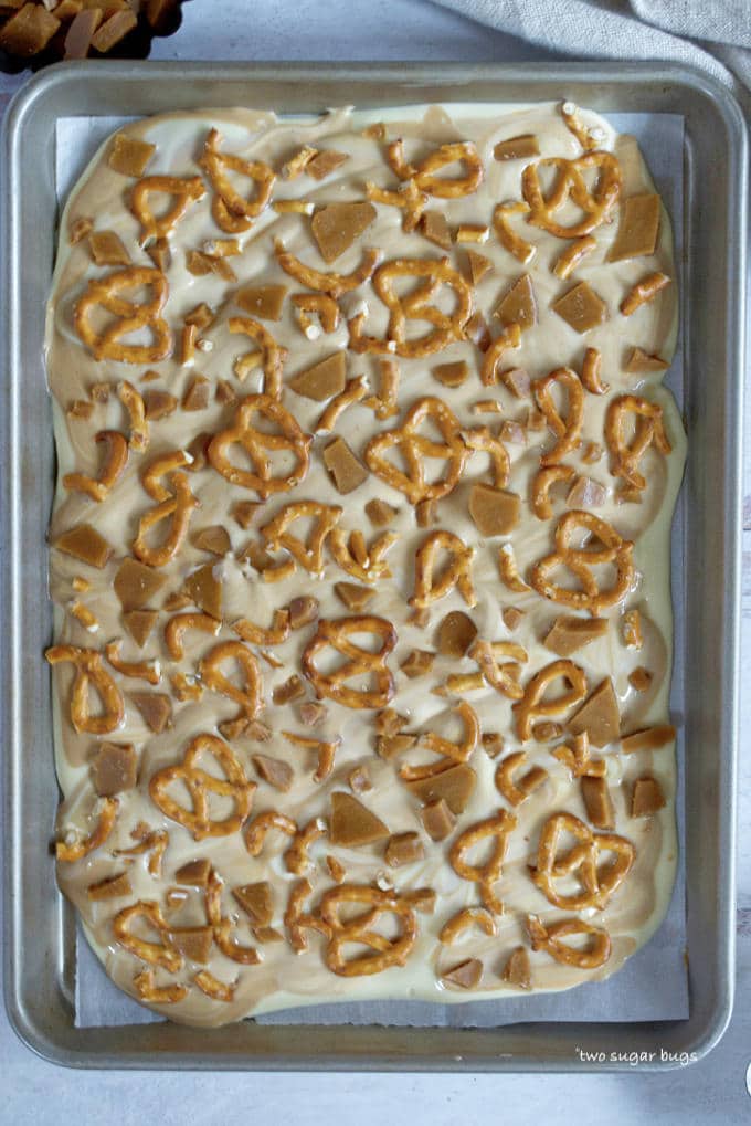 melted white chocolate and cookie butter spread on a baking sheet with pretzels and toffee