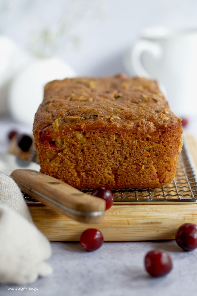 baked loaf of cranberry zucchini bread on a cutting board with a knife