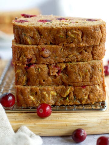 a stack of whole wheat cranberry zucchini bread slices on a cutting board