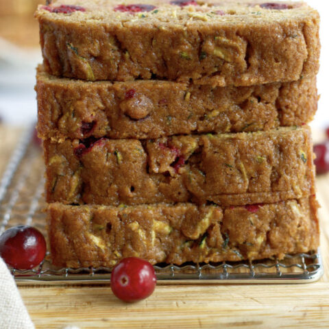a stack of whole wheat cranberry zucchini bread slices on a cutting board