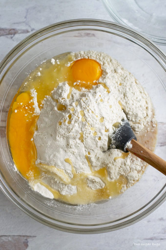 flour, eggs and oil in a bowl on top of milk, yeast and sugar