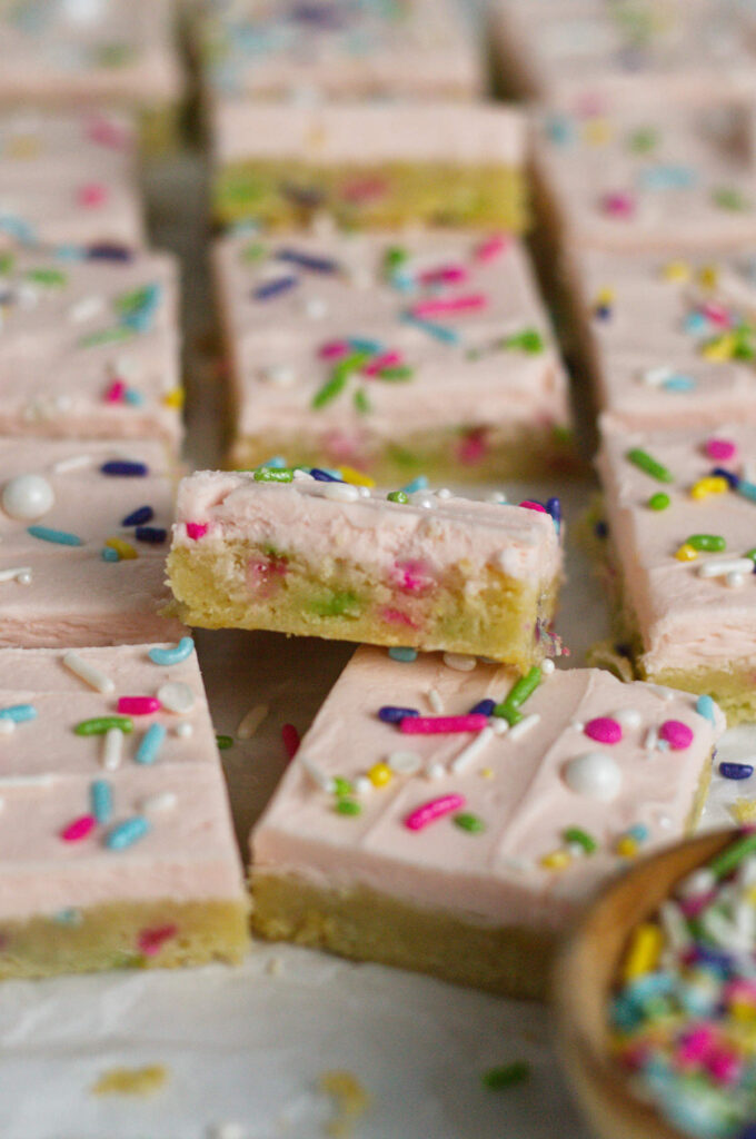 buttercream sugar cookie bars with sprinkles on parchment paper