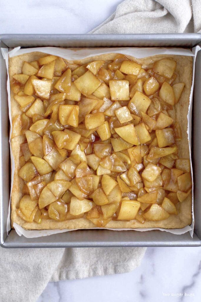 apple filling over shortbread crust in a baking pan
