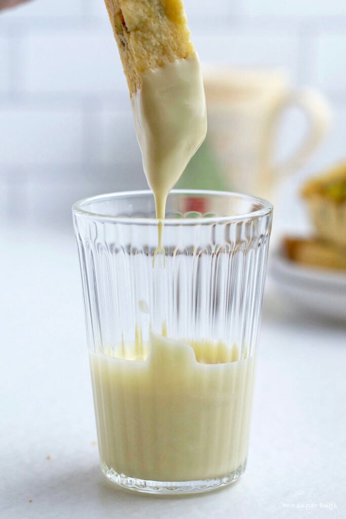 one biscotti being dipped in a glass of melted white chocolate