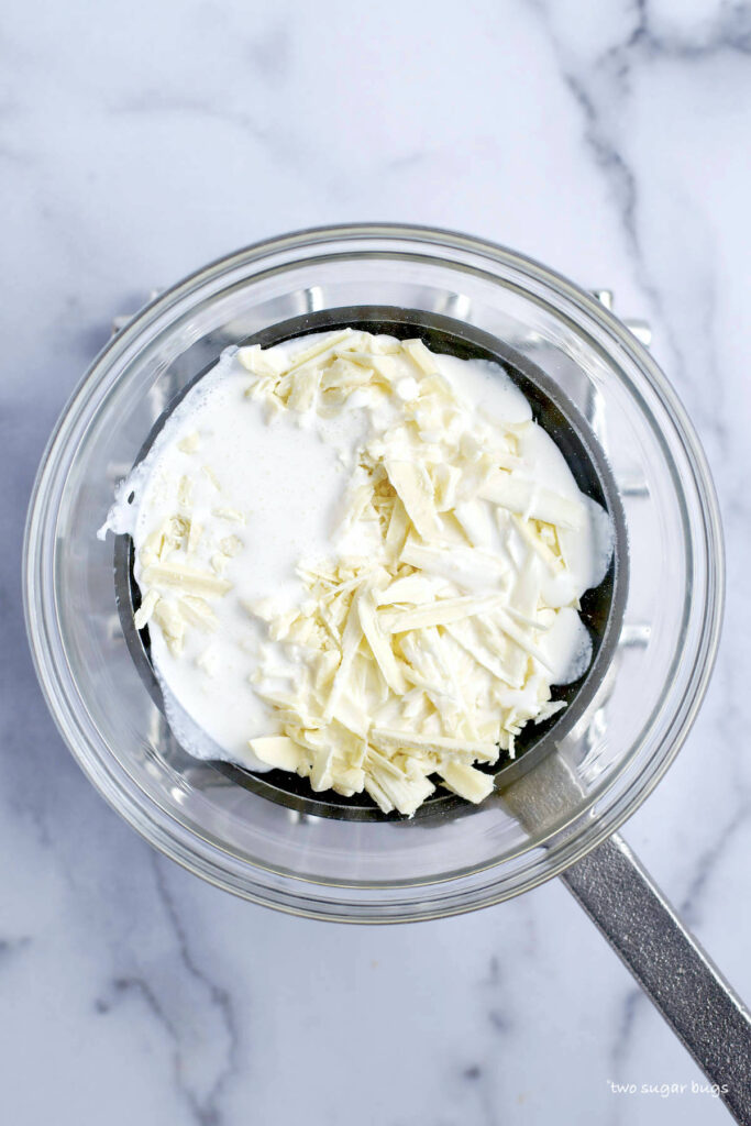 chopped white chocolate and heavy cream in a bowl over a saucepan