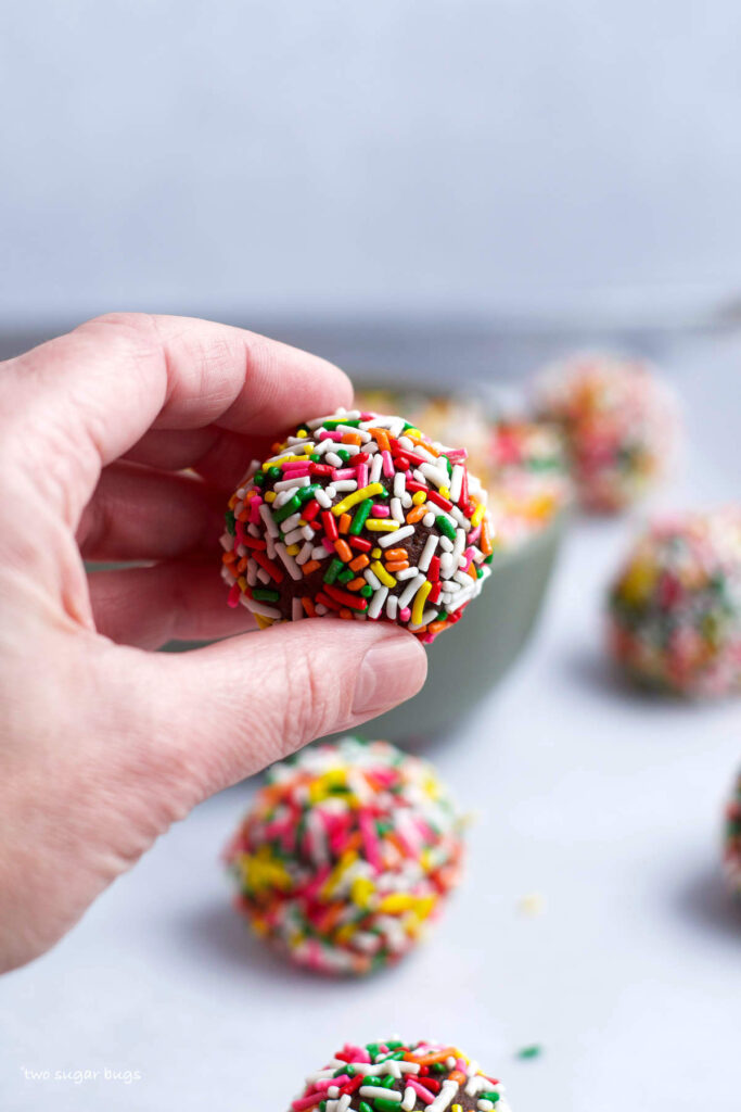 hand holding a rainbow sprinkle filled cookie dough ball