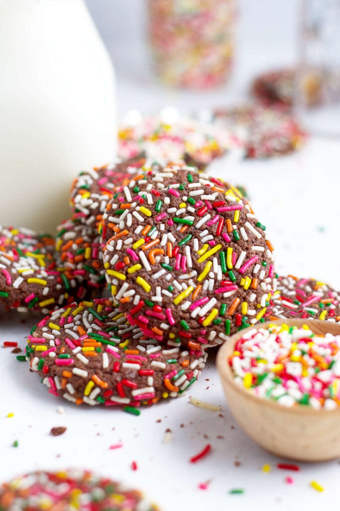 pile of chocolate sprinkle cookies with milk and a bowl of sprinkles