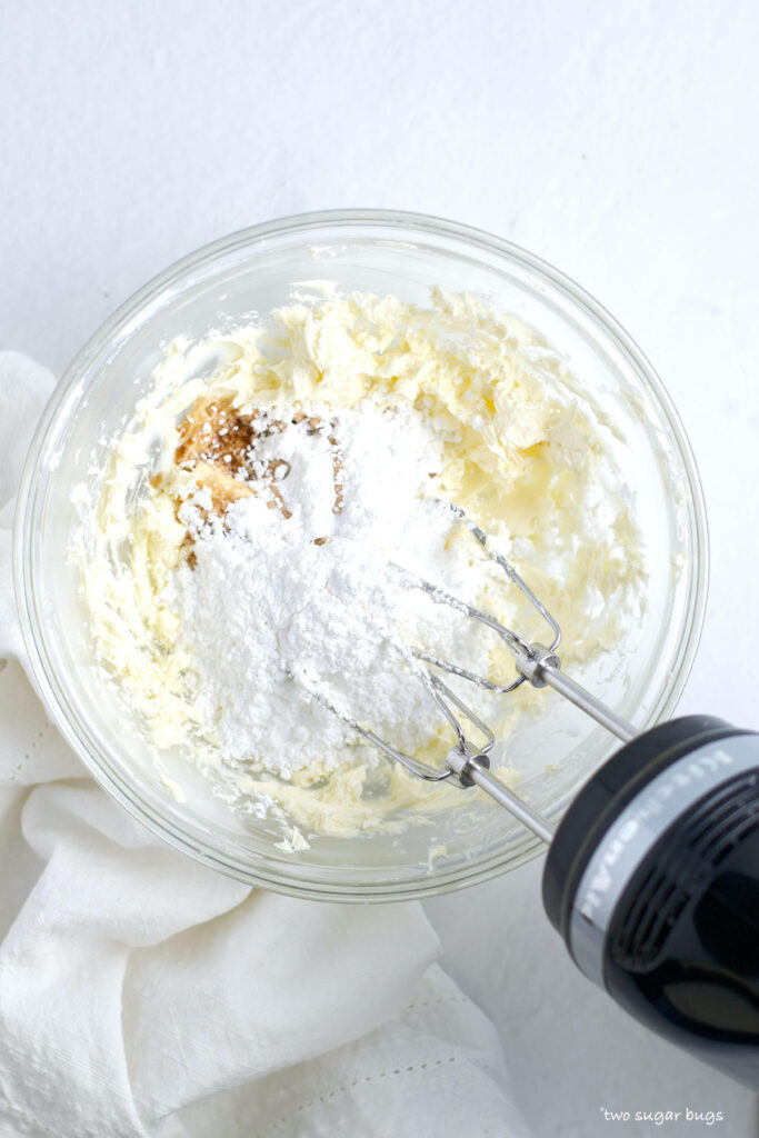 cream cheese frosting ingredients in a bowl with a hand held mixer
