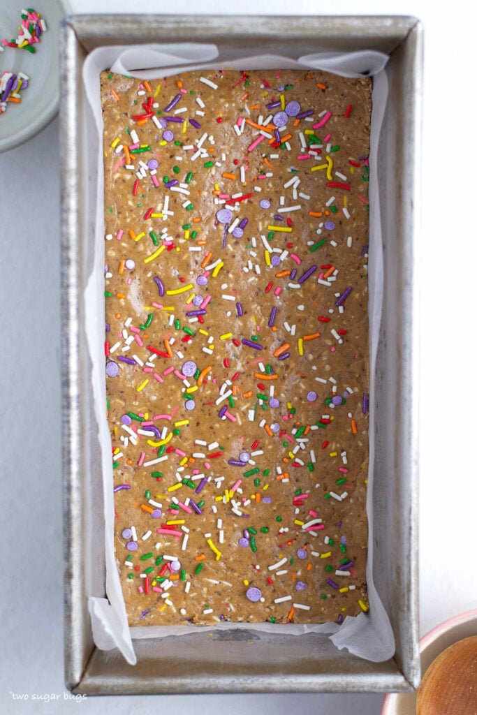 homemade protein bars with sprinkles in a parchment lined baking pan
