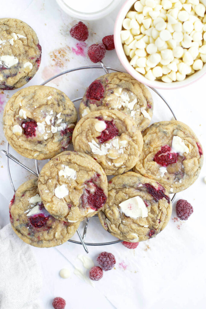 pile of cookies on a cooling rack with a glass of milk and white chocolate chips