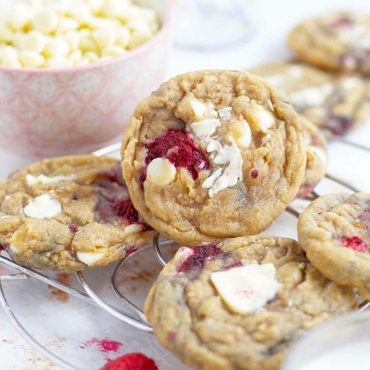 white chocolate raspberry cookies on a cooling rack with a bowl of white chips in the background