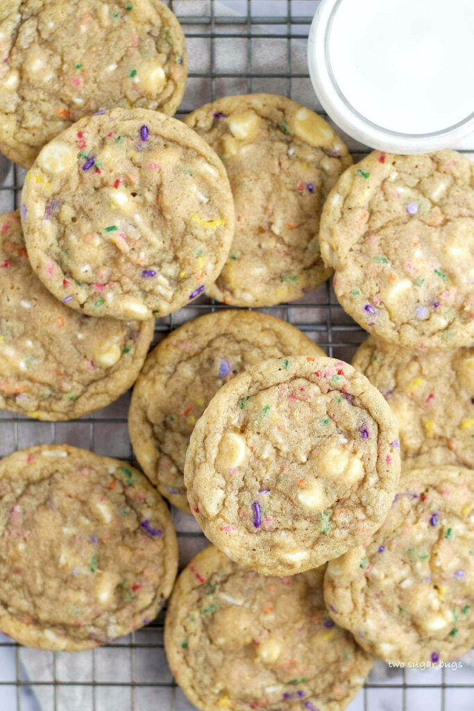 a pile of birthday cake cookies on a cooling rack with milk
