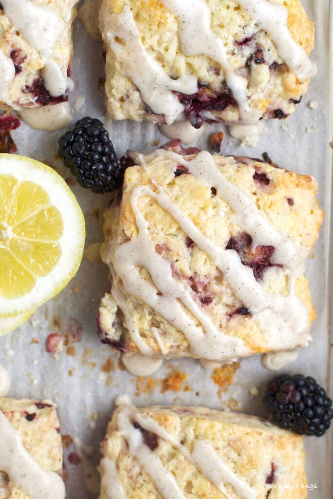 baked scones on a baking sheet with fresh lemons and blackberries