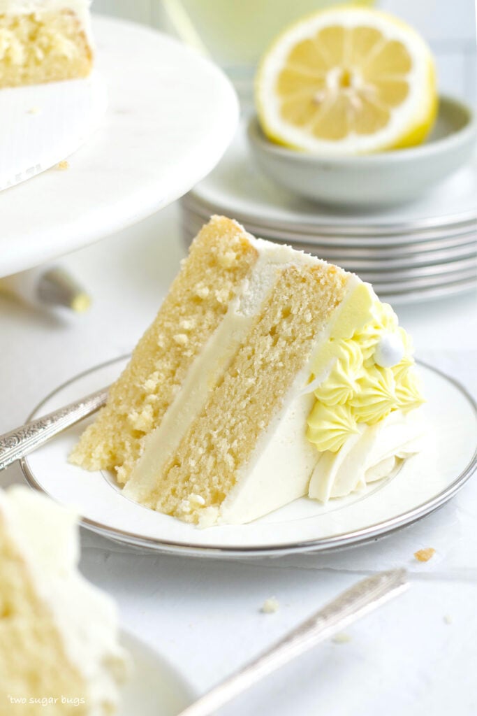slice of lemon white chocolate cake on a plate with a pile of plates in the background