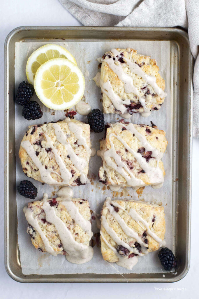 five blackberry lemon scones on a baking sheet with lemons and blackberries