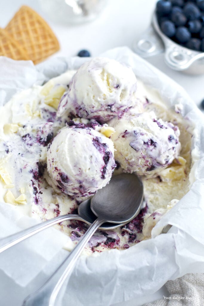 scoops of white chocolate ice cream in the ice cream pan with a bowl of blueberries
