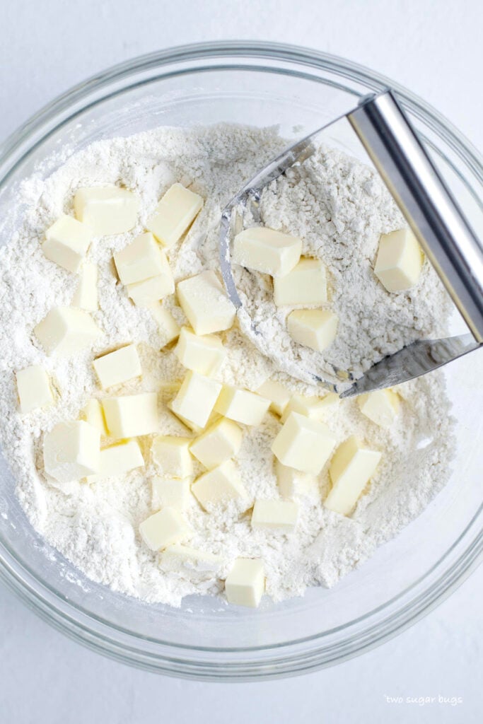 butter added to dry ingredients in a bowl with a pastry cutter
