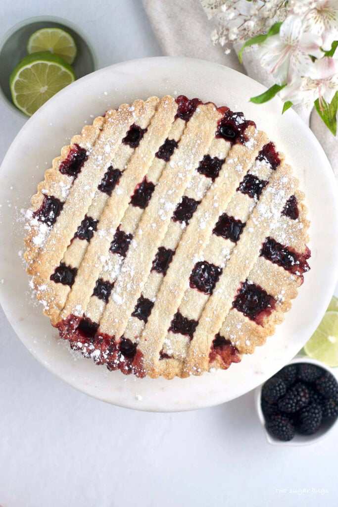 blackberry crostata on a serving plate with a cup of blackberries and limes