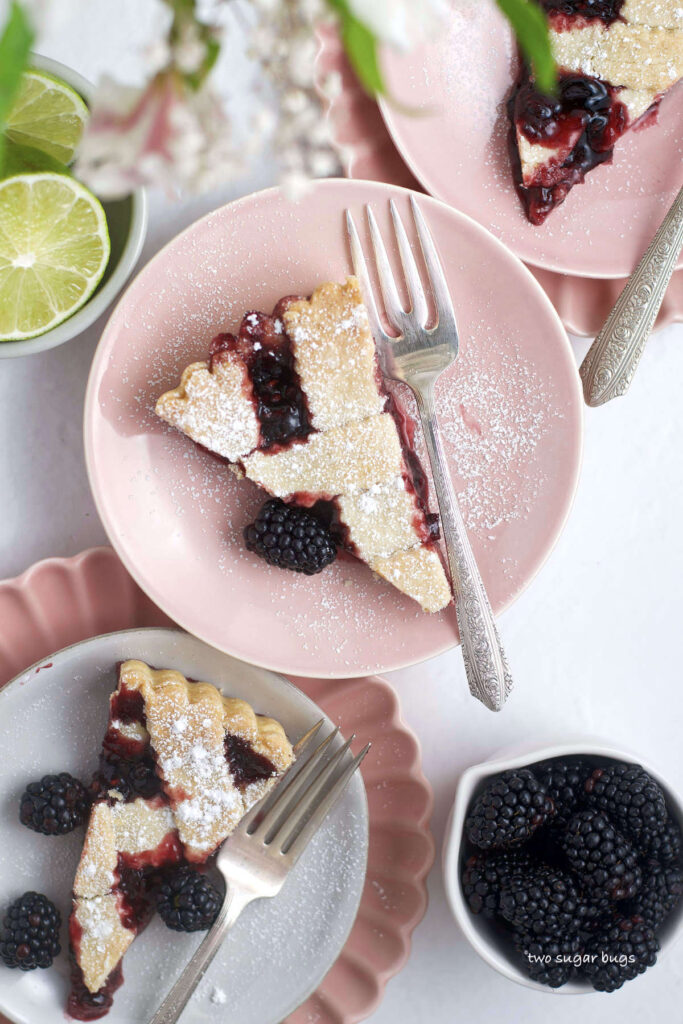 three slices of blackberry crostata on plates with forks