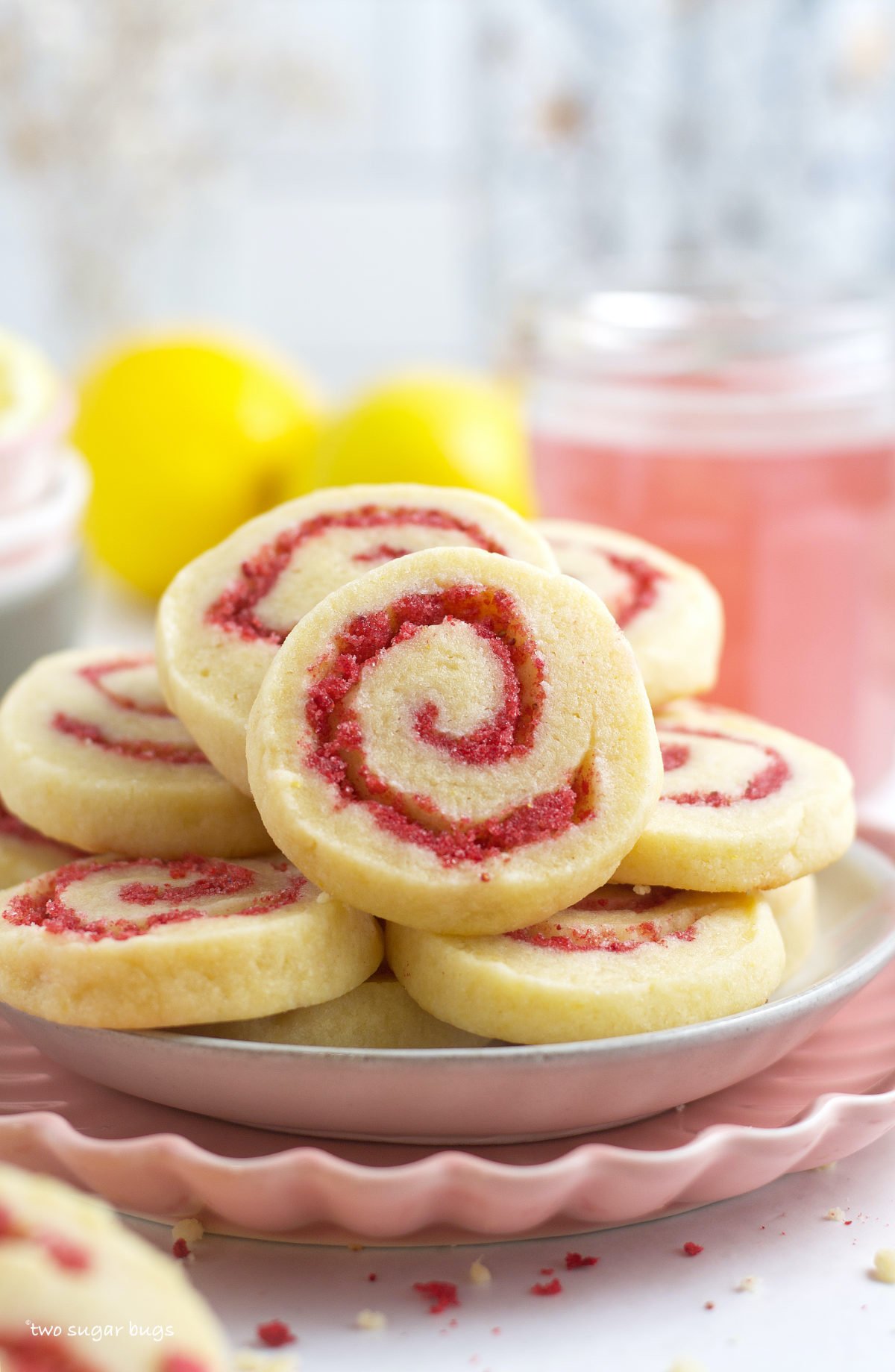 sugar cookies piled on a plate with a glass of strawberry lemonade