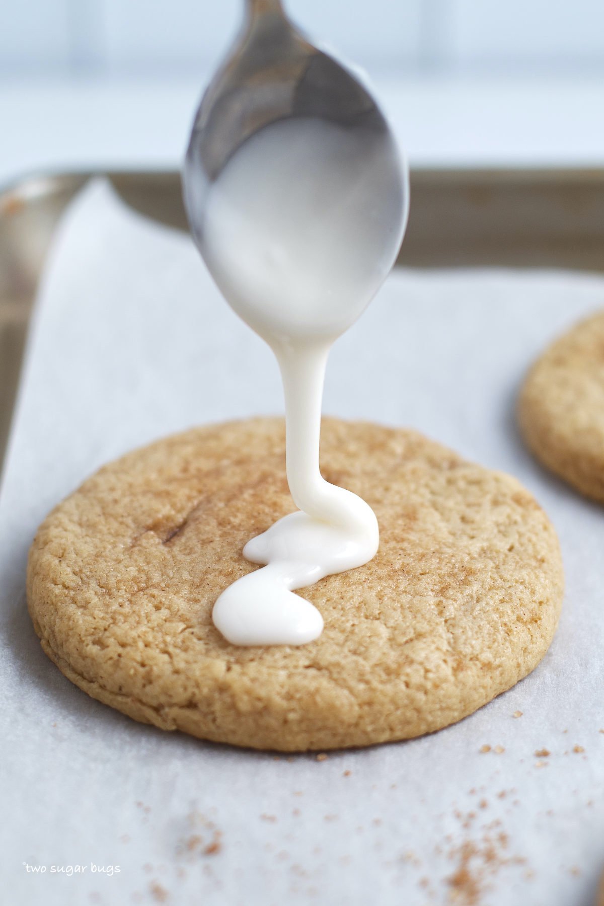 spoon drizzling vanilla frosting on a cookie