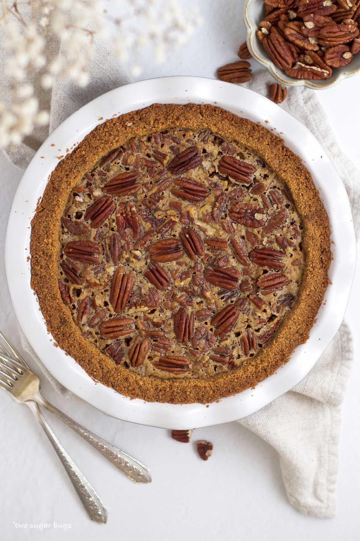 baked pecan pie with a bowl of pecans and forks