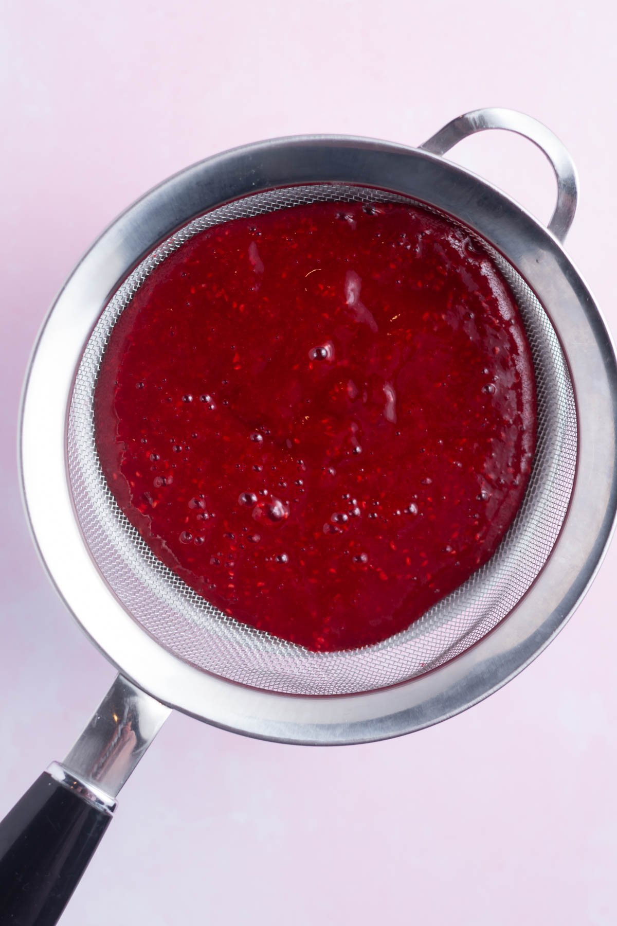 raspberry puree being pushed through a sieve