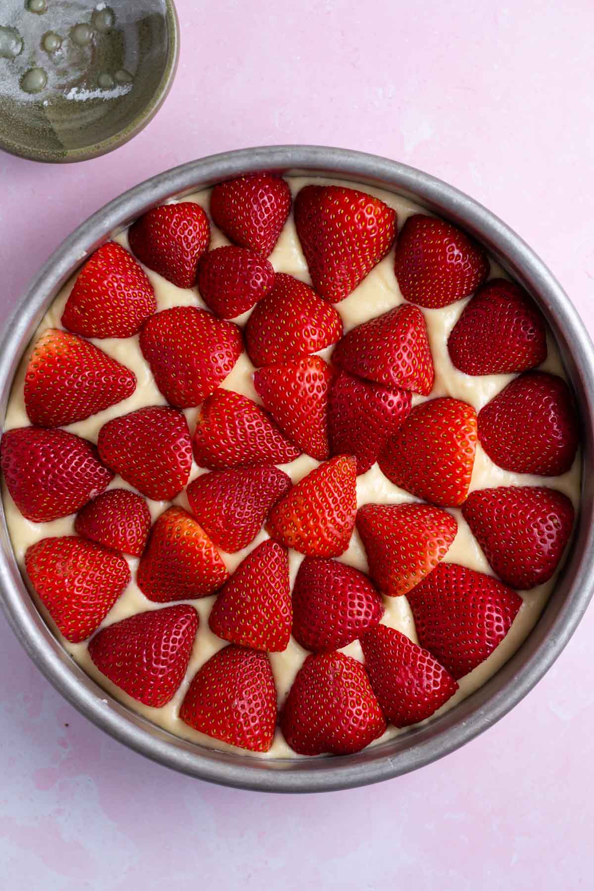 fresh strawberries layered over vanilla cake batter in a baking pan