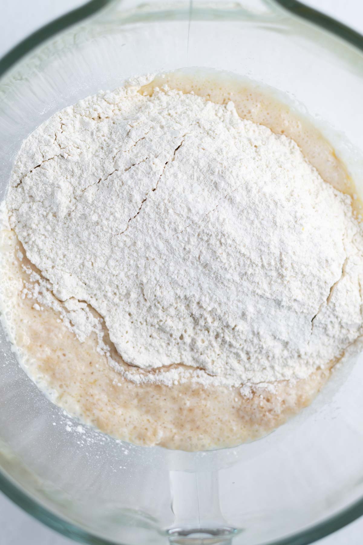 flour added on top of activated yeast, sugar and melted butter in a mixing bowl
