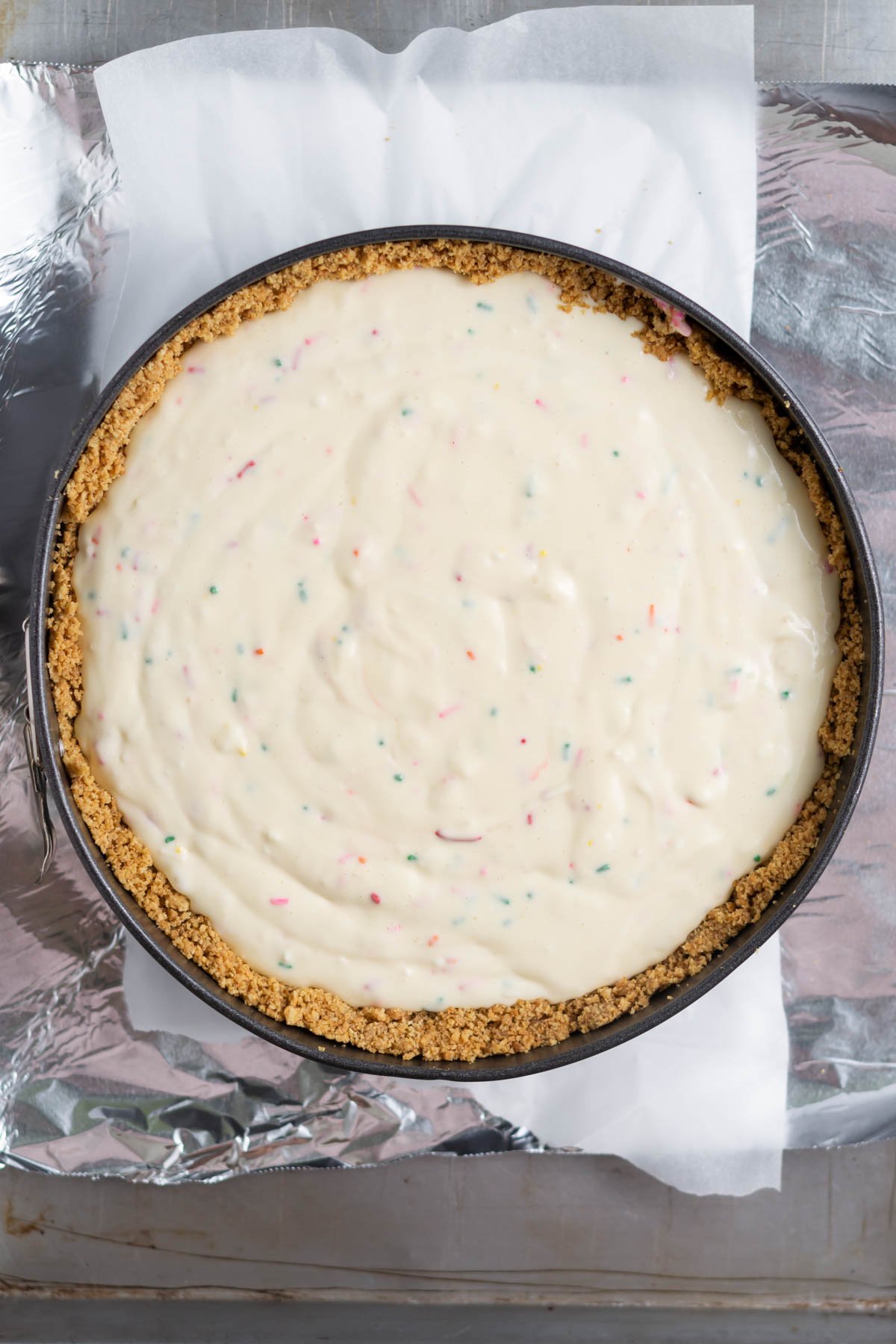 birthday cheesecake batter in a springform pan on a foil lined baking pan