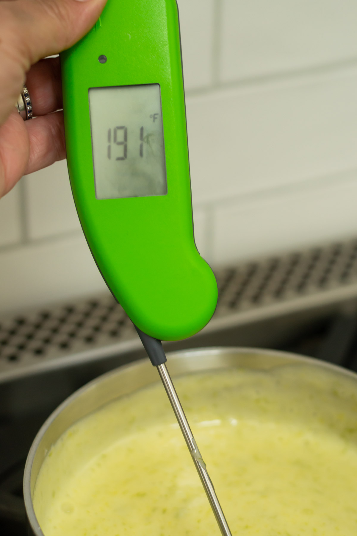 hand holding a thermometer showing curd cooked to a high enough temperature