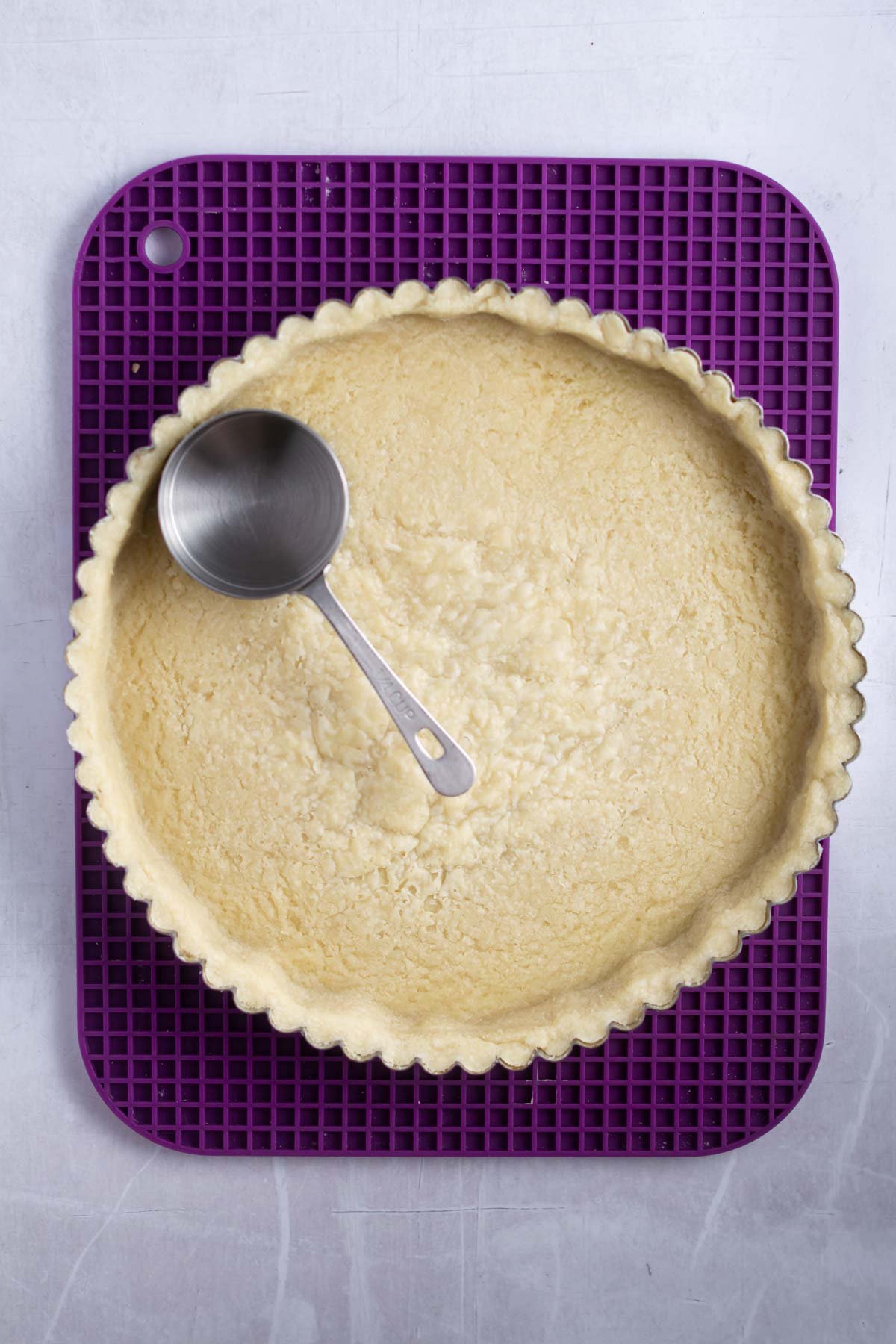 par baked shortbread crust with a measuring cup showing how to flatten the bottom