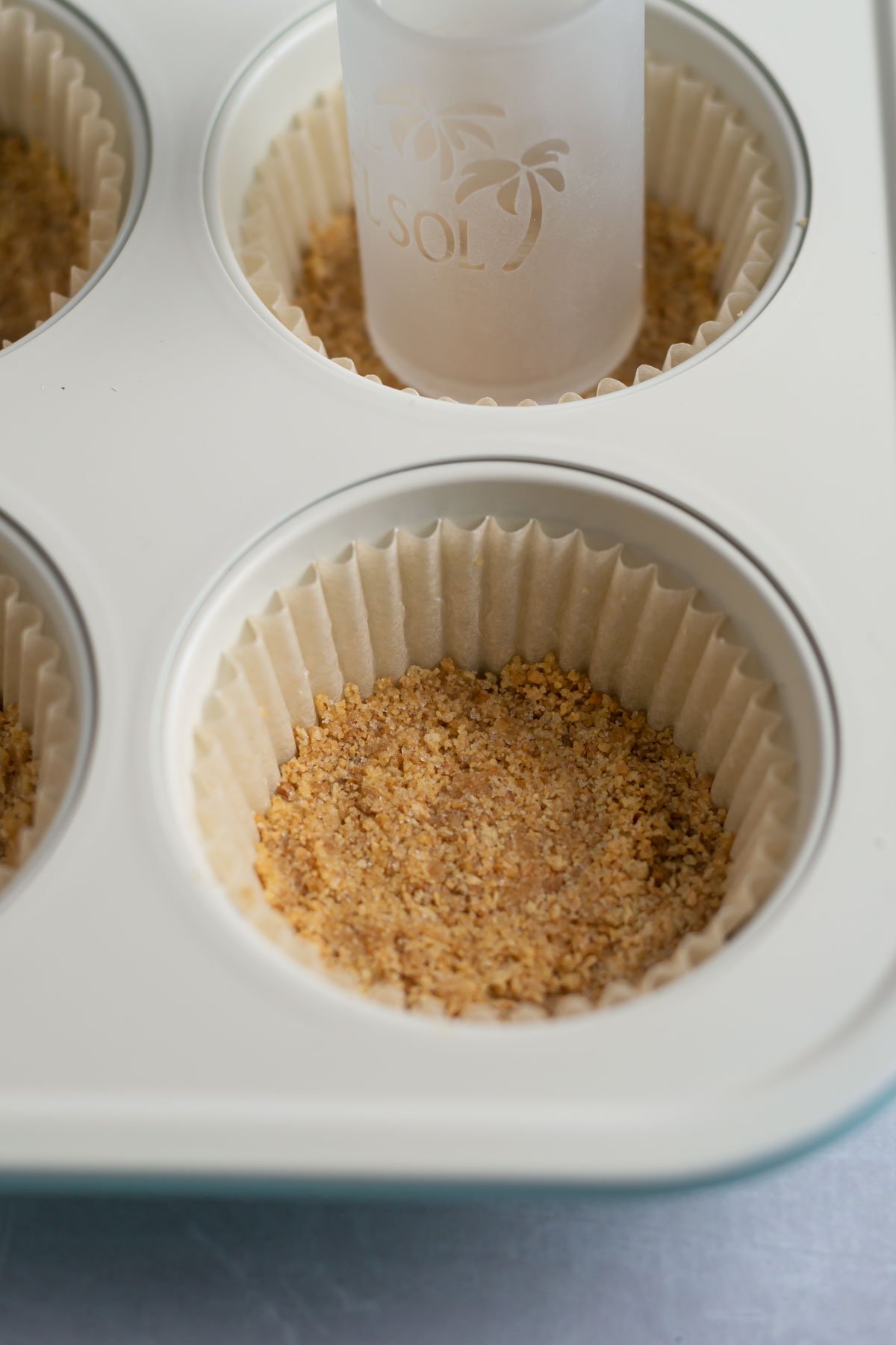 shot glass pressing graham cracker crust into muffin liners