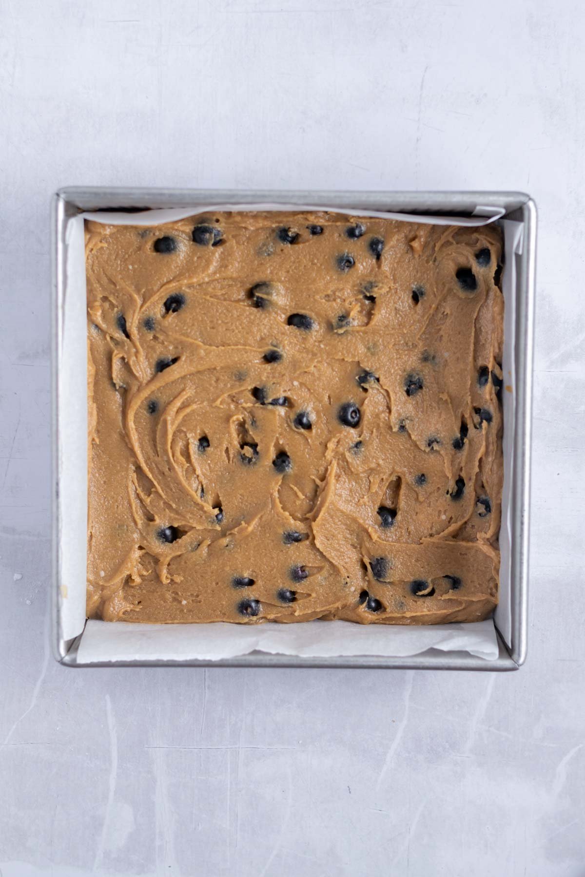 blueberry blondie batter in a parchment lined baking pan.