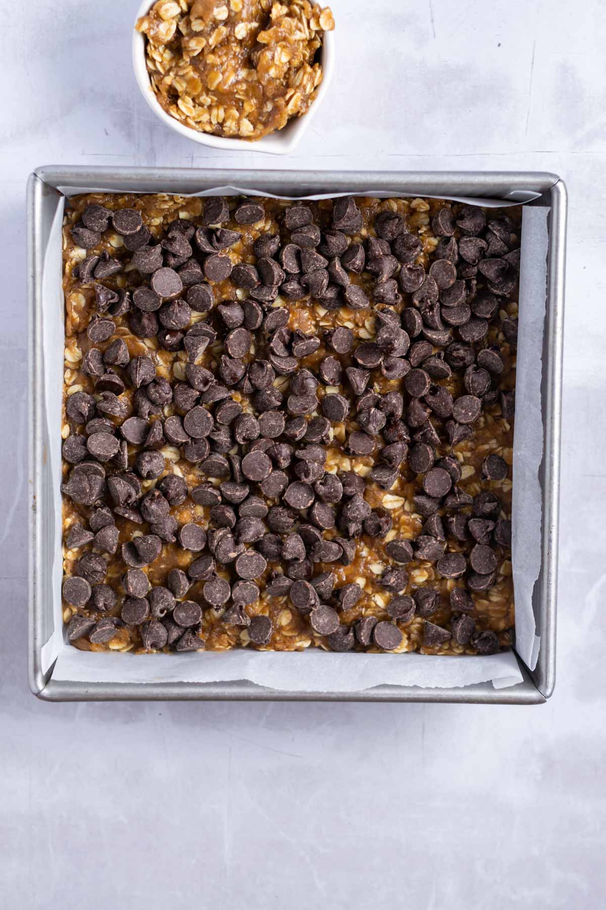 chocolate chips spread over oatmeal base layer in a baking square