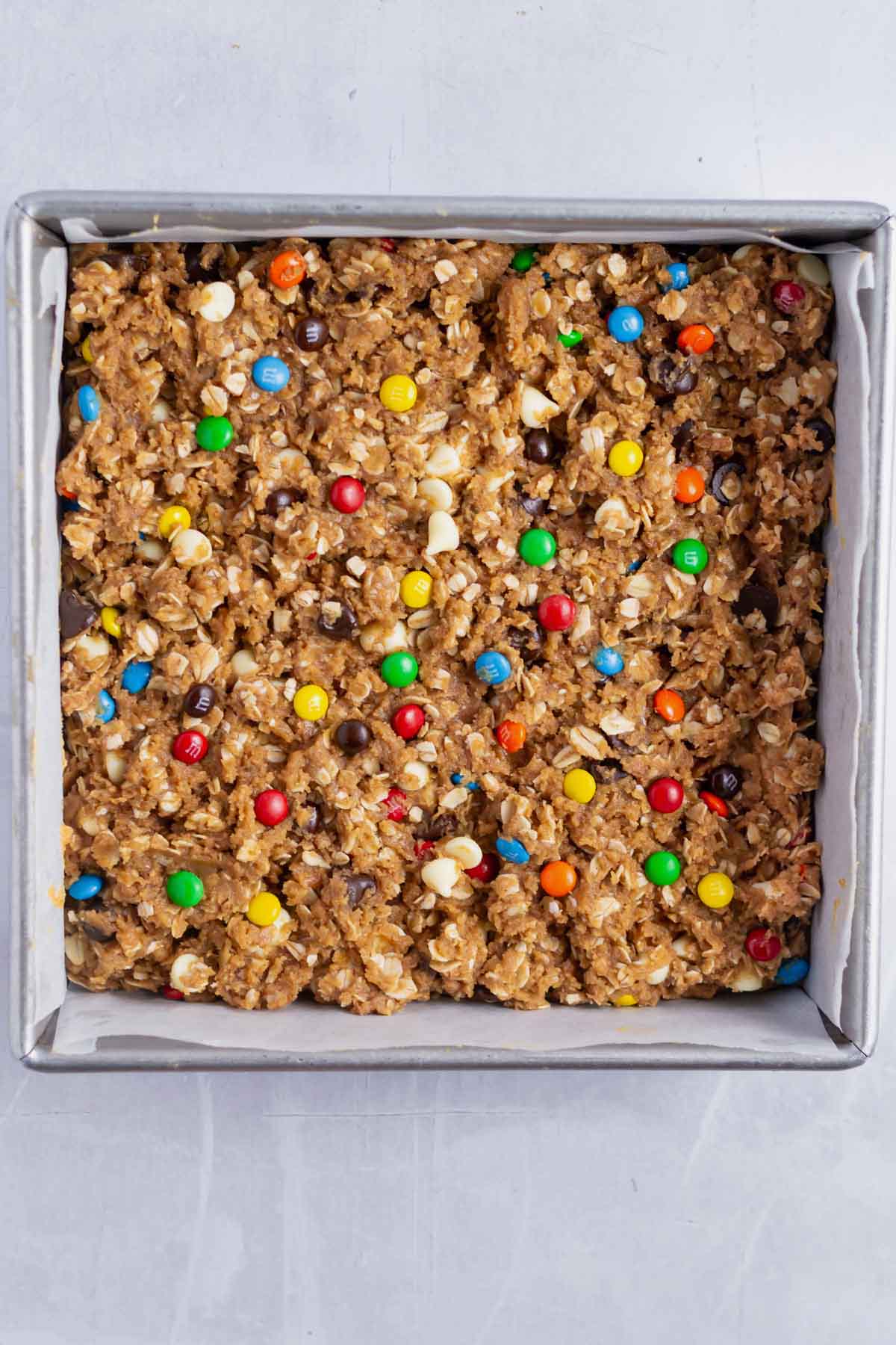 unbaked monster cookie bars in a parchment lined baking pan