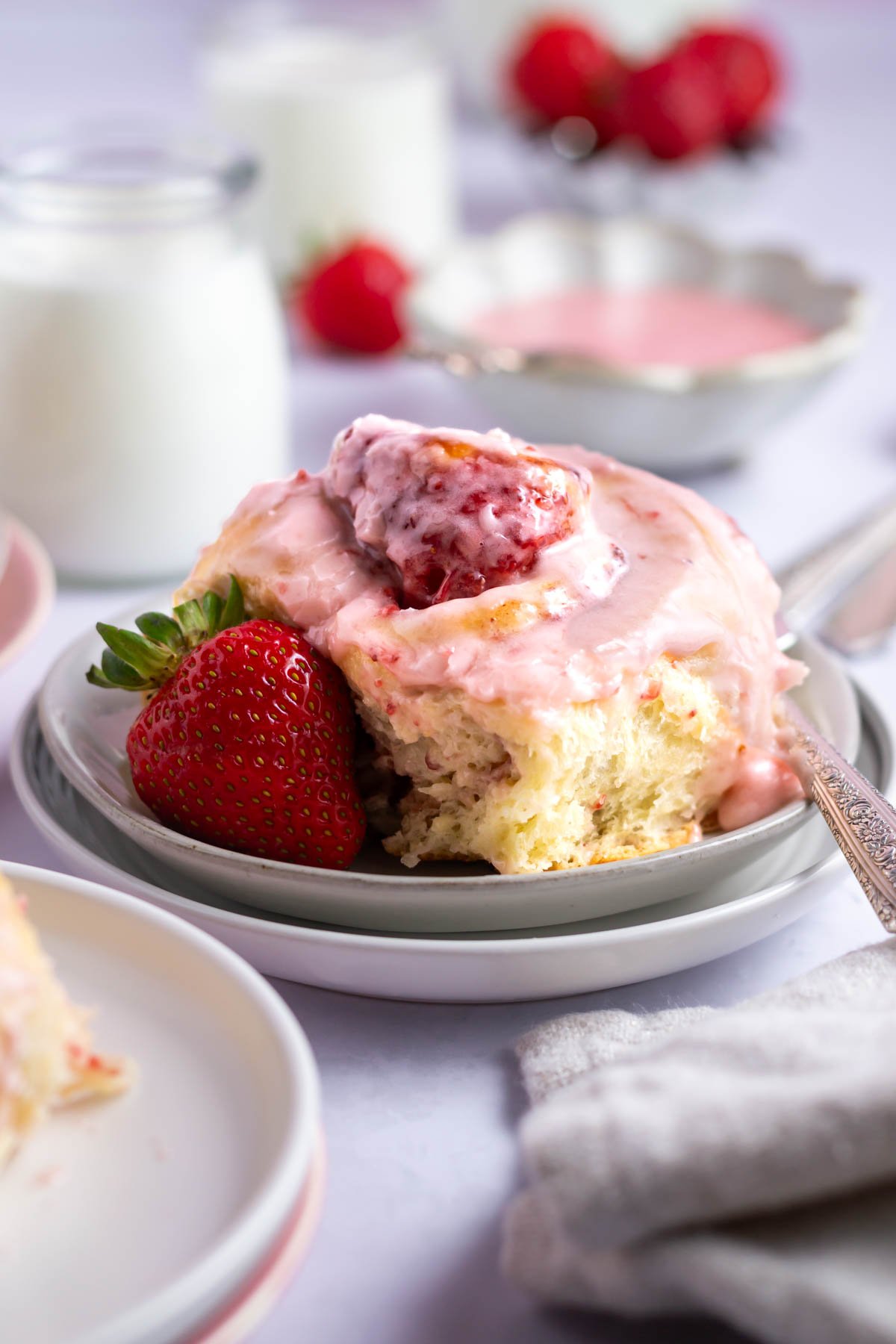 strawberry cinnamon roll on a plate with a fresh strawberry