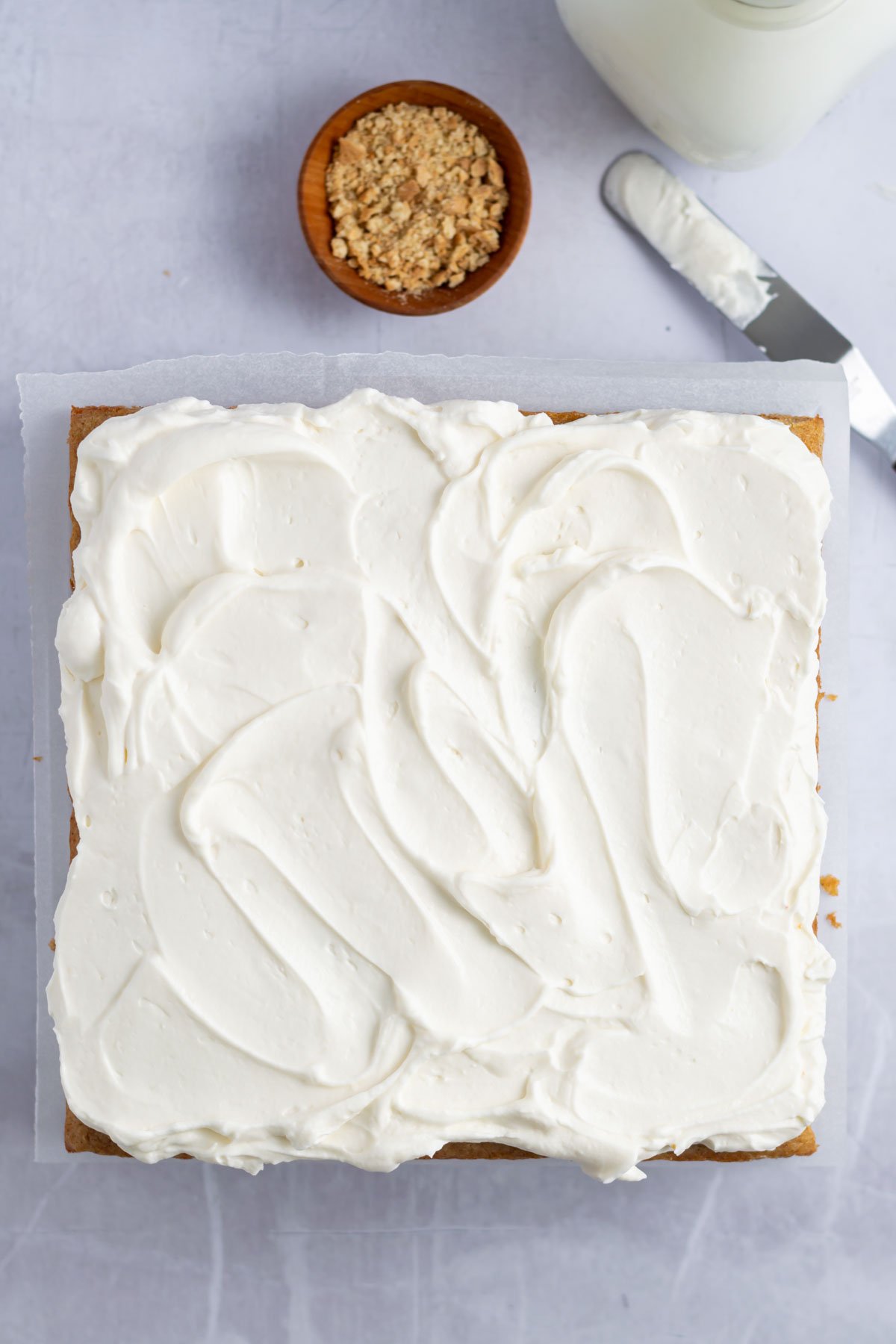 frosting topping swirled on top of cake with a bowl of graham cracker crumbs
