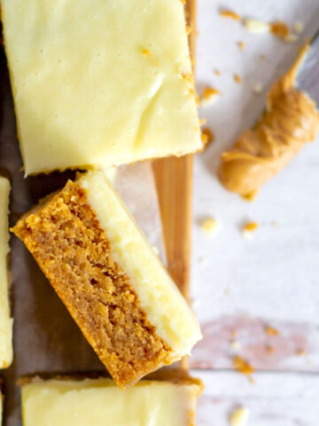 peanut butter blondie with white chocolate ganache on it's side on a cutting board
