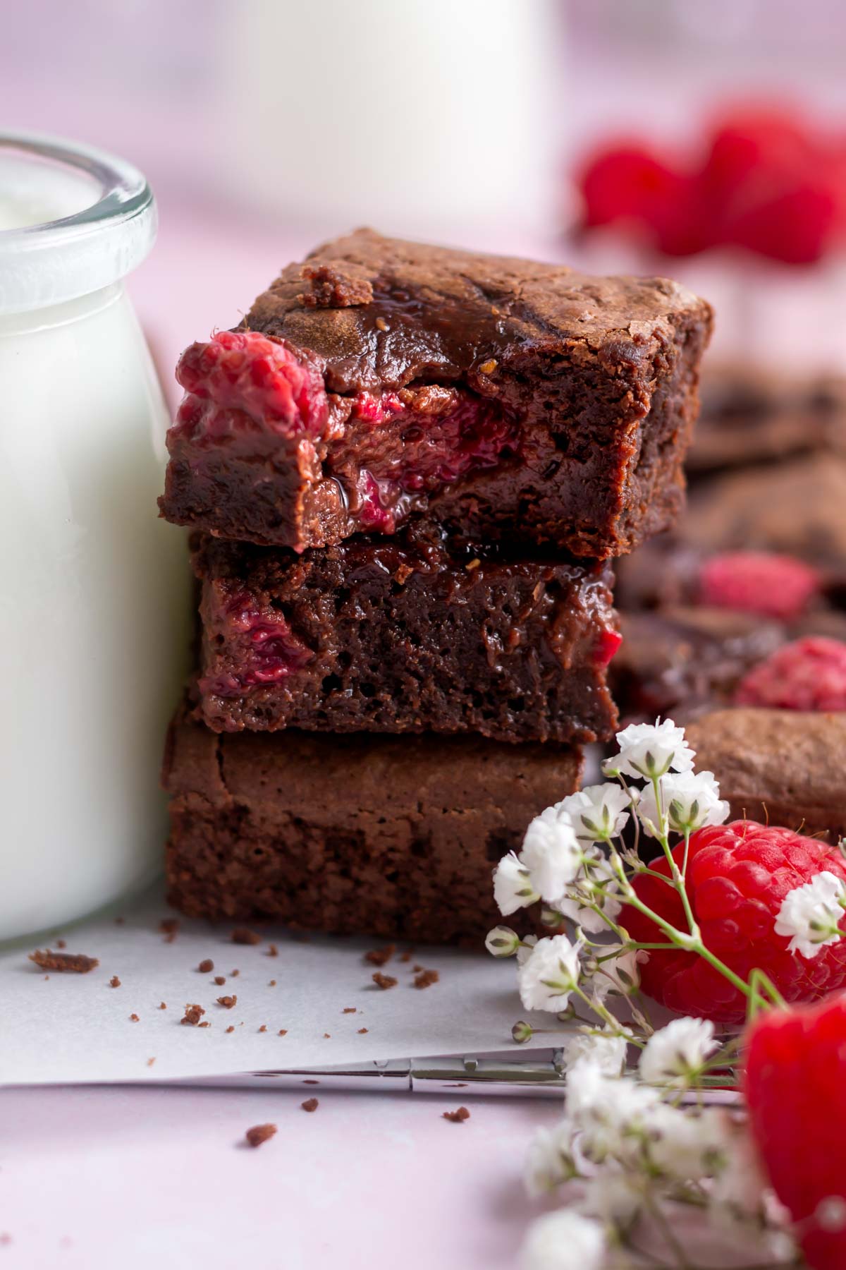 raspberry brownie with a bite missing in a stack with milk and fresh raspberries and flowers