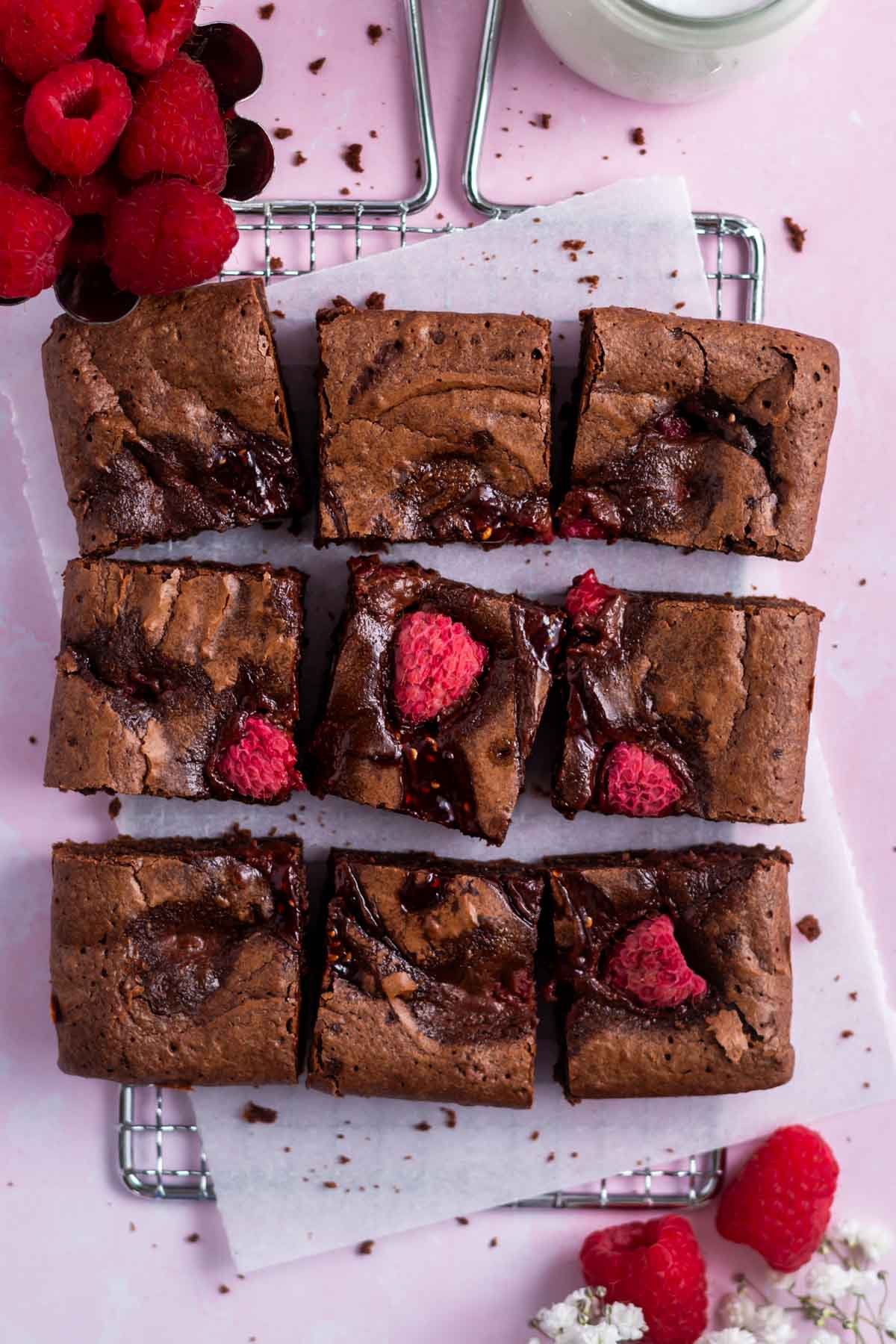 raspberry brownies on a parchment lined cooling rack with fresh raspberries and milk