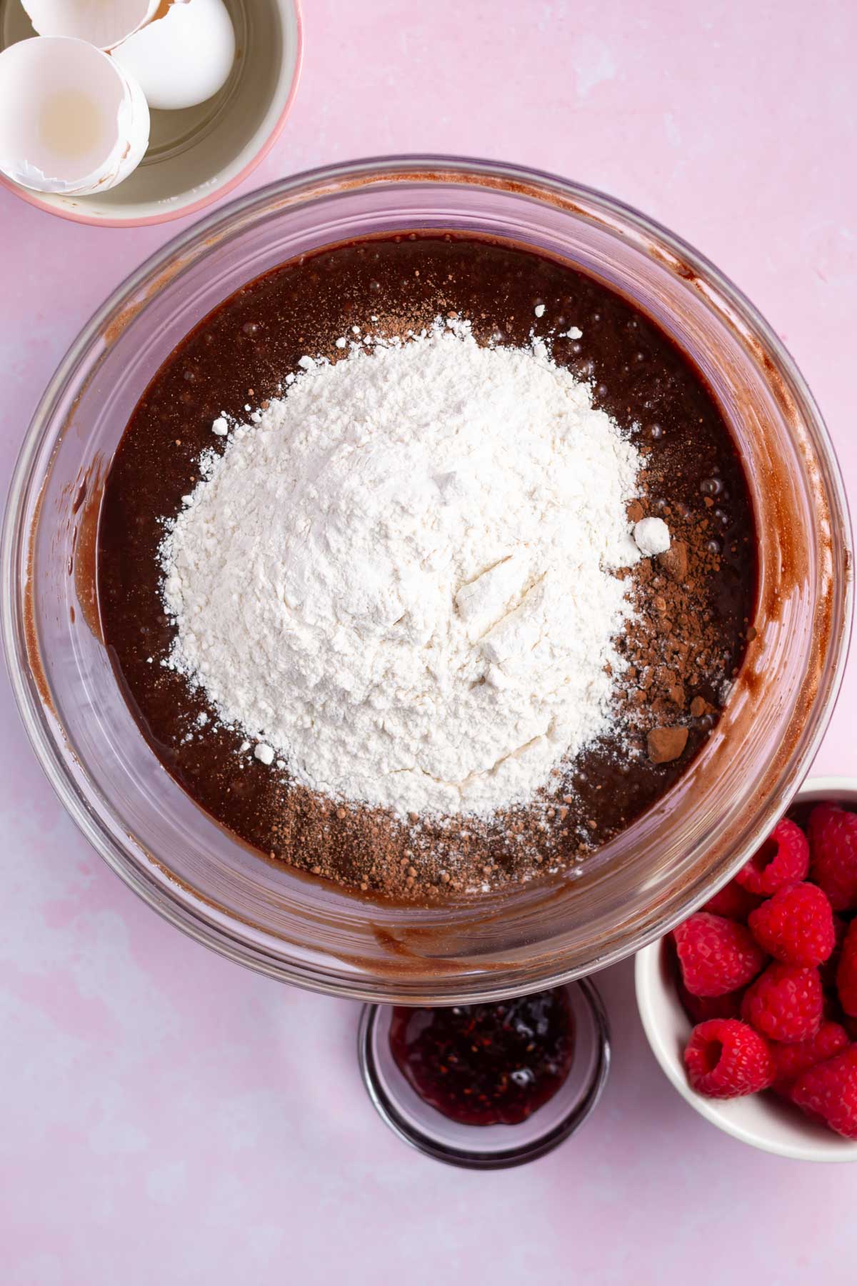 cocoa powder and flour added on top of the brownie batter in a bowl